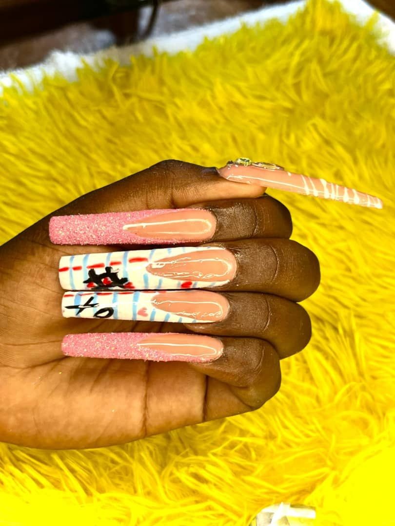 Hand displaying long, colorful nail art with designs and glitter, on a yellow background.