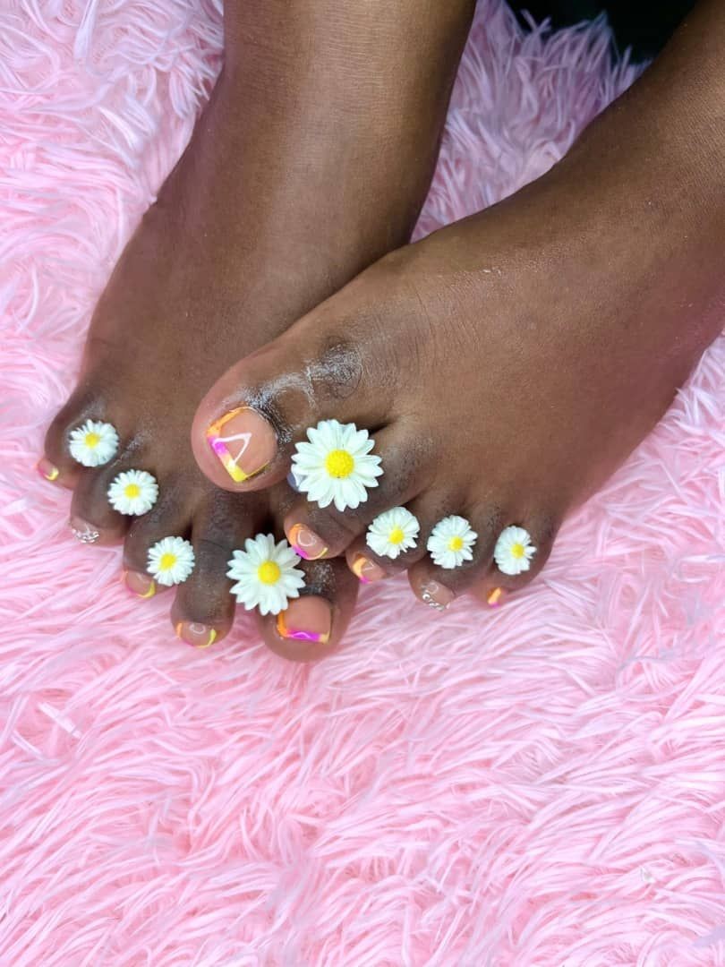 Feet with daisy flowers on nails, resting on a pink fluffy surface.